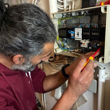 Elektriker von Elektro Breyer & Veron GmbH prüft eine Elektroinstallation in einem geöffneten Schaltschrank.