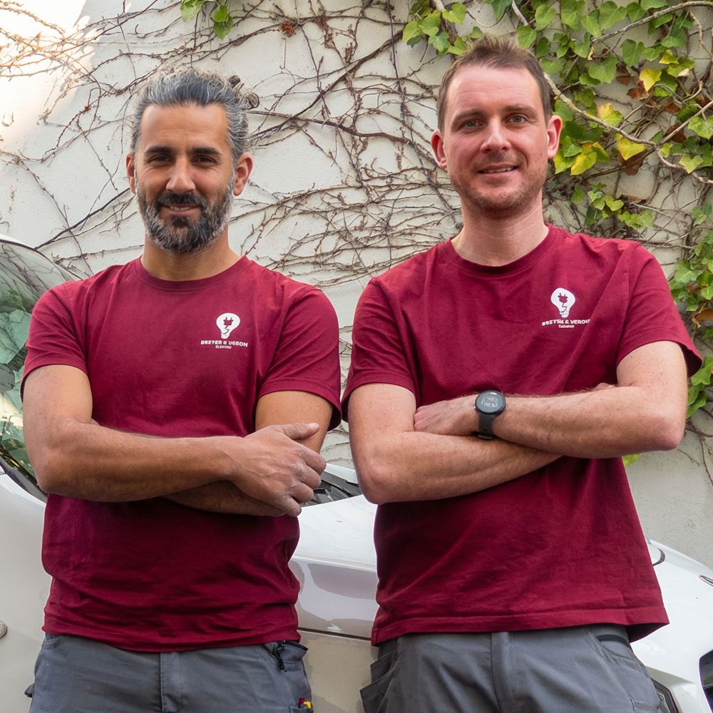 Denis Breyer und Tolga Veron von Elektro Breyer & Veron GmbH im Porträt vor einer Wand mit Ranken.